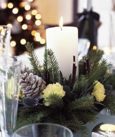 černobílé vánoční ozdoby se stříbrnou a forstovanou fialkou pro domácnost, jídelní stůl se svíčkou uprostřed z čerstvě řezané větve, šišky a karafiáty