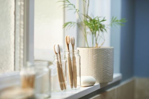 plastové dřevěné dřevěné zubní kartáčky zdarma ve skleněné nádobě vedle dalších produktů s nulovým odpadem na okenním parapetu v koupelně