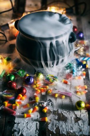 vysoký úhel pohledu na hrnec s kouřem uprostřed rozptýlených bonbónů na stole během halloweenu