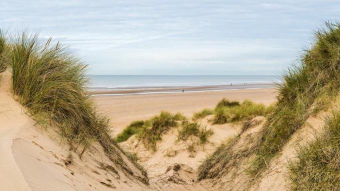 vícesnímkové panoráma zachycené mezi dvěma vrcholy na písečných dunách shlíží na lidi, kteří jdou po formby beach poblíž liverpoolu