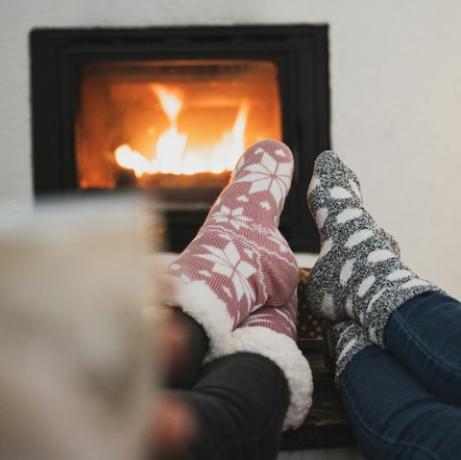 pohled zezadu na dvě přítelkyně sedící u krbu a vánoční stromeček s nohama se zimními ponožkami na konferenčním stolku, popíjející kávu nebo čaj