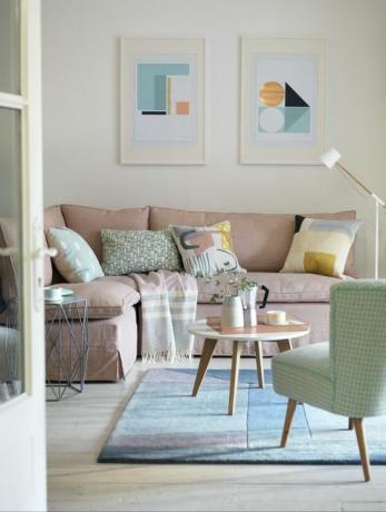 bílý obývací pokoj se světle růžovou pohovkou, malým kulatým konferenčním stolkem, modrým kobercem, zeleným křeslem a obrazy na stěně