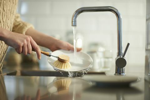 žena používá kartáč bez plastu k čištění nádobí v kuchyňském dřezu, zblízka