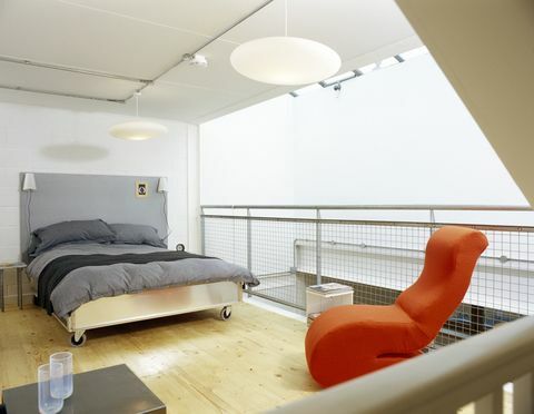 Moderní ložnice s šedou přikrývkou a zářivě oranžovou židlí