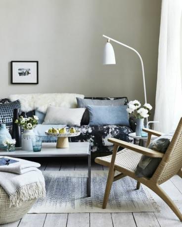 neutrální obývací pokoj, obývací pokoj s polštáři na modré vzorované pohovce, ohnutá bílá stojací lampa nad pohovkou kape, skvrny a stříkající vzory pro animpresionistický vzhled, který je současný a uvolněný
