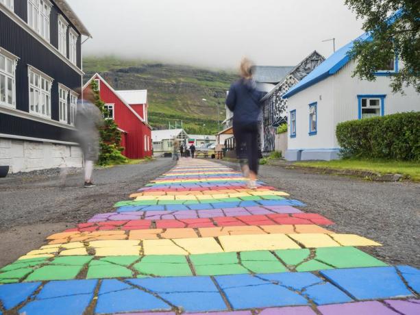 Island, seydisfjordur, lidé jdoucí po duhově zbarvené asfaltové silnici uprostřed odlehlého města