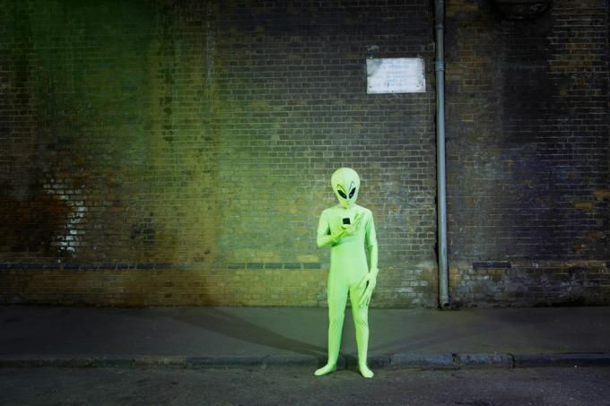 muž oblečený v kostýmu mimozemšťana při pohledu na mobil