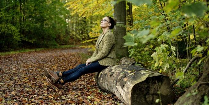 zralá žena sedící na kmeni stromu v podzimním lese