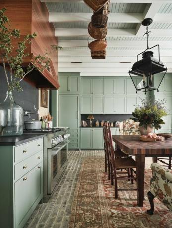 kuchyně, zelené skříně, plošný koberec, dřevěný jídelní stůl s dřevěnými židlemi, dřevěná digestoř, zeleň
